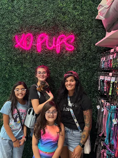 Group posing with a puppy beneath the XO Pups sign